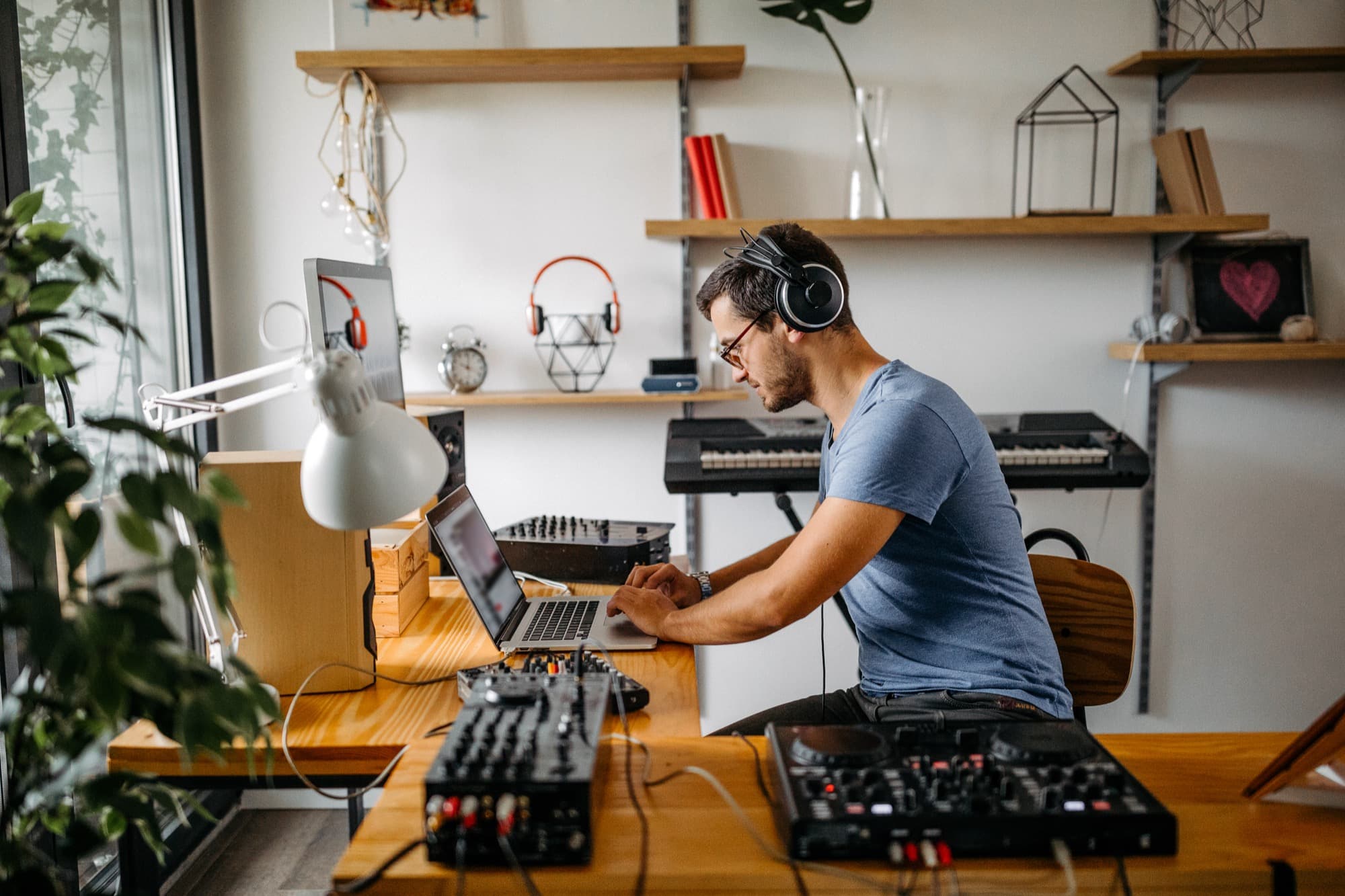 A producer at a home studio with DJ controllers, MIDI keyboard, mixer, and laptop — the kind of setup you already work in.